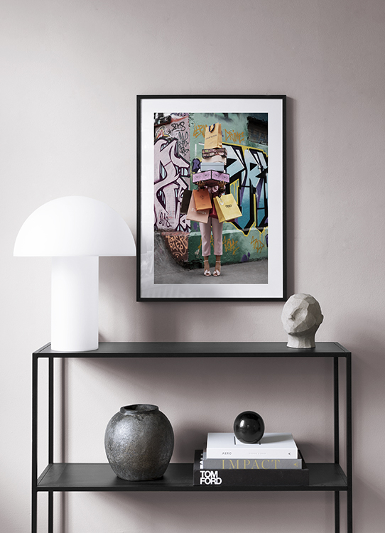  – Fotografia di una donna che tiene in mano una pila di shopping bag e scatole di scarpe, davanti a una parete con murales