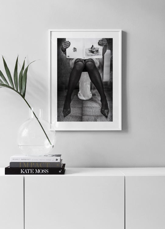  – Photographie en noir et blanc d’une femme assise sur les toilettes et lisant un magazine