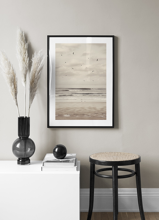  – Fotografia di una spiaggia e un oceano con uccelli neri che volano in un cielo nuvoloso